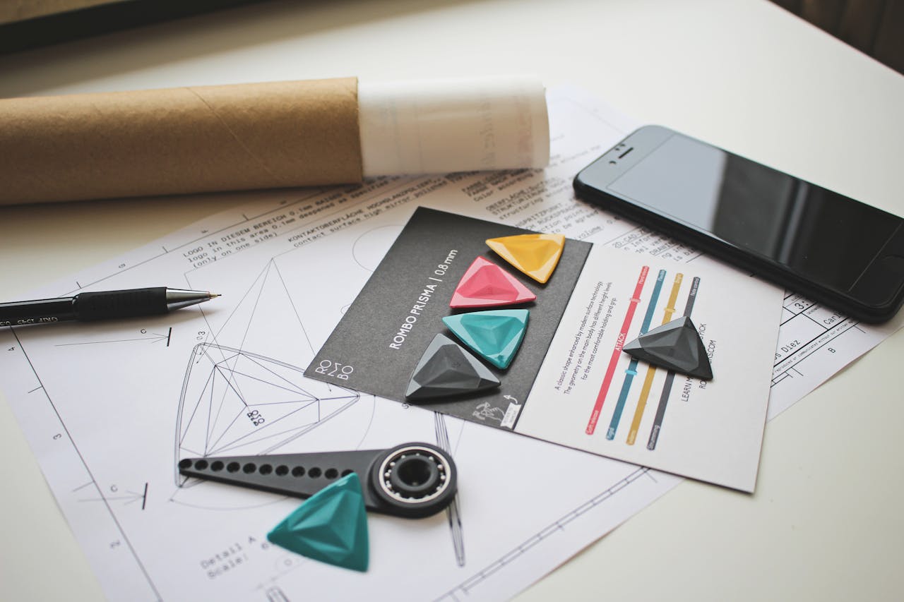A creative workspace with guitar picks, design plans, and a smartphone on a white table.